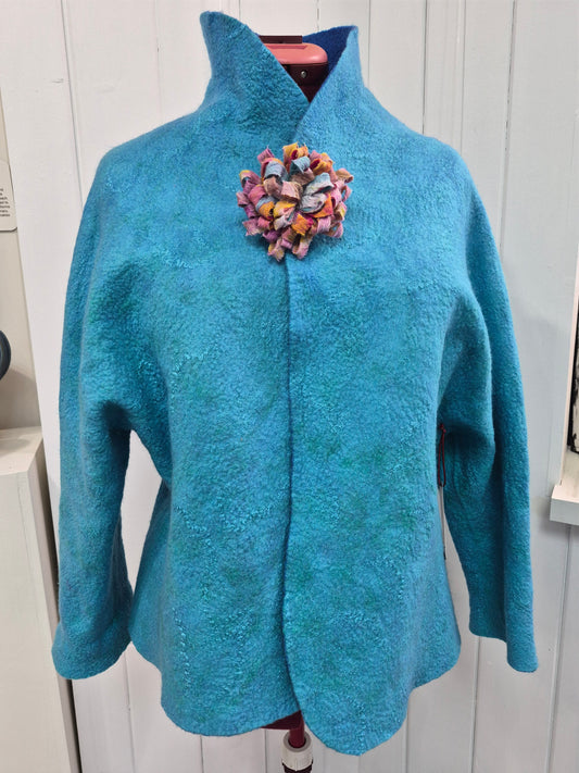 Turquoise-blue textured jacket by Denise Uebele with long sleeves and a standing collar, shown with a floral accessory