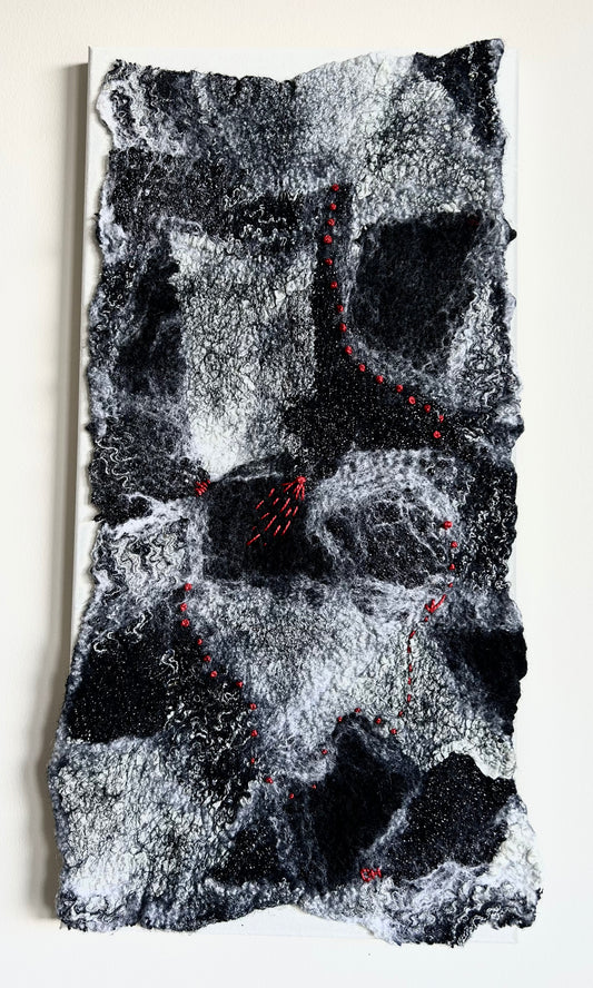 Full vertical view of black, white, and grey nuno-felted fibre art with red stitching, displayed on a light wall.